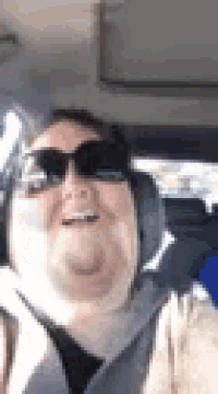 a woman wearing sunglasses and headphones is smiling while sitting in a car .