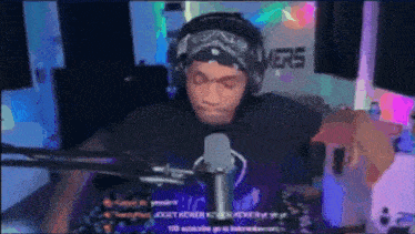 a man wearing headphones and a bandana stands in front of a microphone in a room with the word gamers on the wall