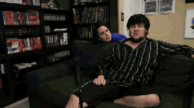 two men are sitting on a couch in front of bookshelves