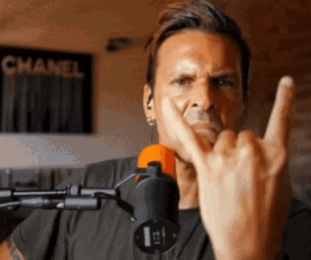 a man in front of a microphone is making a horns sign