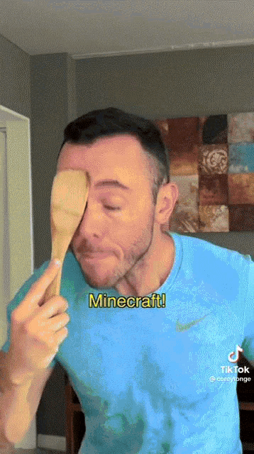 a man in a blue shirt is holding a wooden spoon in front of his face with minecraft written on the bottom