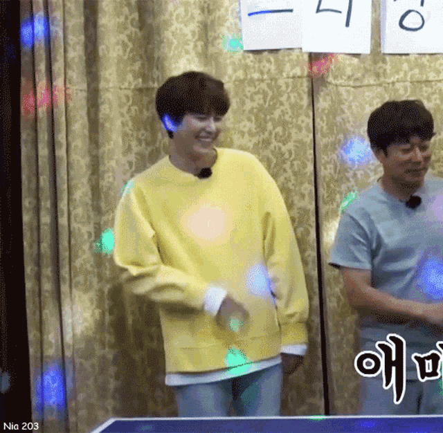 a man in a yellow sweater is standing next to another man in a grey shirt