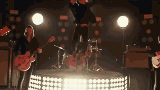 a group of people are playing guitars and drums on a stage