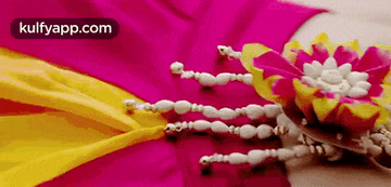 a close up of a pink and yellow cloth with a flower and beads on it