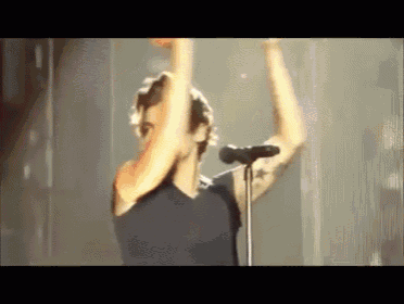 a man is singing into a microphone with his arms in the air on a stage .