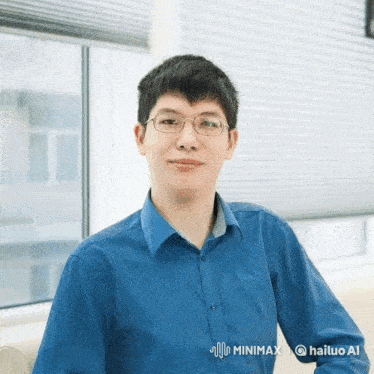 a man wearing glasses and a blue shirt is standing in front of a window with hailuo ai written on the bottom