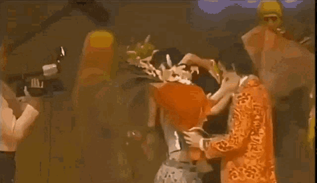 a group of people are dancing in a dark room and one of them is wearing a yellow jacket