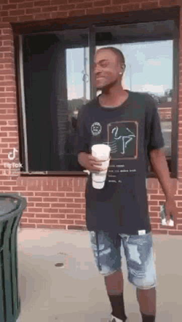 a man is standing in front of a brick building holding a coffee cup .