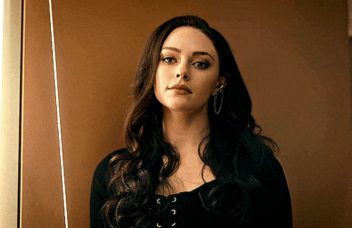 a woman with long dark hair and hoop earrings is standing in front of a wall .