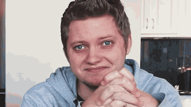 a young man with his hands folded looks at the camera