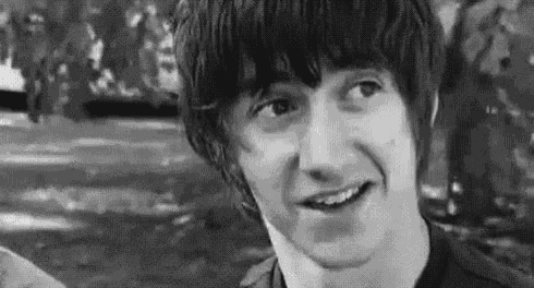 a black and white photo of a young man smiling in a park with trees in the background .