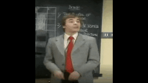 a man in a suit and red tie is standing in front of a chalkboard .