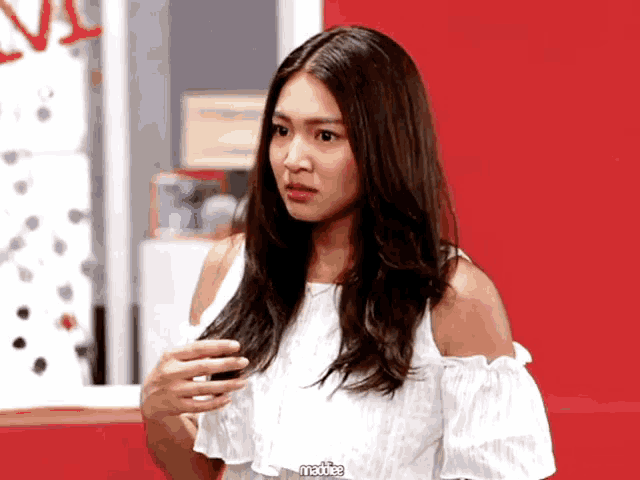 a woman in a white off the shoulder top is standing in front of a red wall with the word maddie written on it