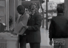a man in a suit with a skull mask on his face is standing in front of a store .