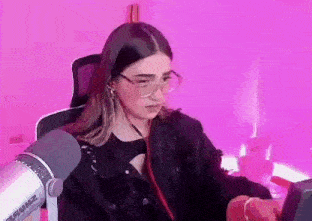 a woman wearing glasses is sitting in front of a microphone in a pink room .