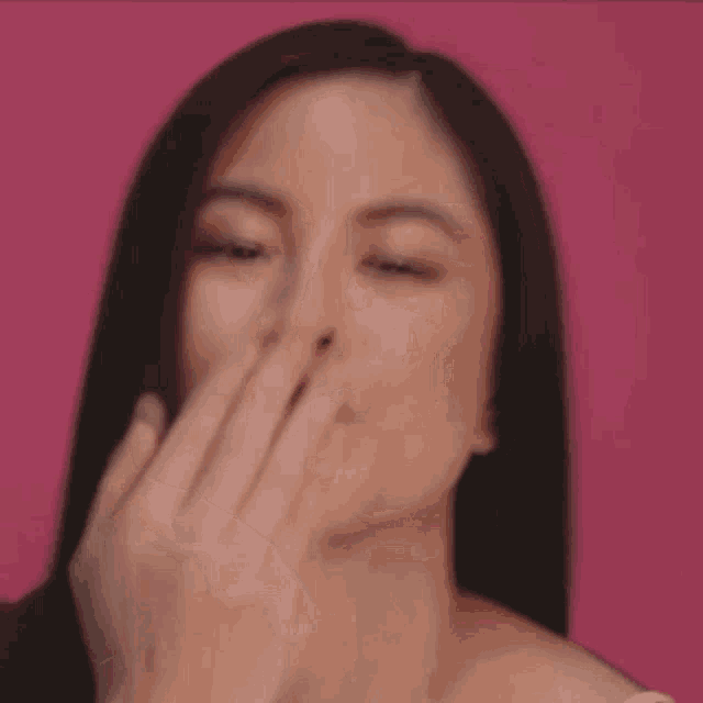a woman is covering her face with her hand against a pink background .
