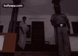 a man in a white shirt is dancing in front of a police officer with the words kulfyapp.com below him