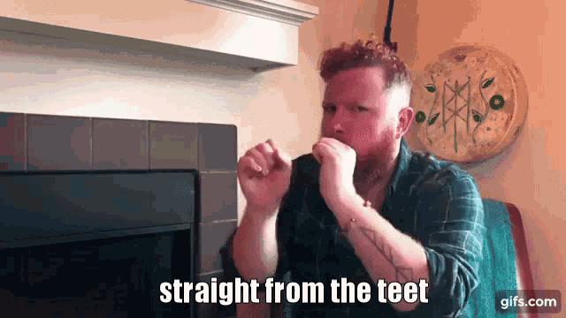 a man with a beard is sitting in front of a fireplace with the words straight from the teet above him