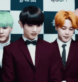 a group of young men wearing suits and bow ties are standing in front of a checkered wall .