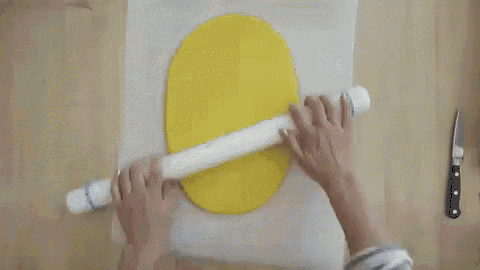 a person is rolling a piece of yellow dough on a piece of wax paper .