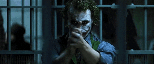 the joker is holding a gun in a jail cell and pointing it at the camera .