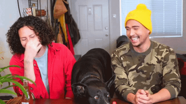 two men are sitting at a table with a dog laying on the table