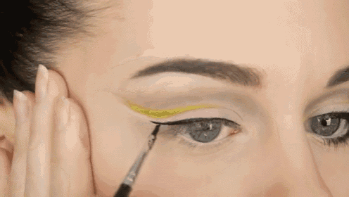 a close up of a woman applying yellow eyeliner to her eye
