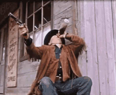 a man in a cowboy hat is kneeling down holding a gun and drinking from a bottle .