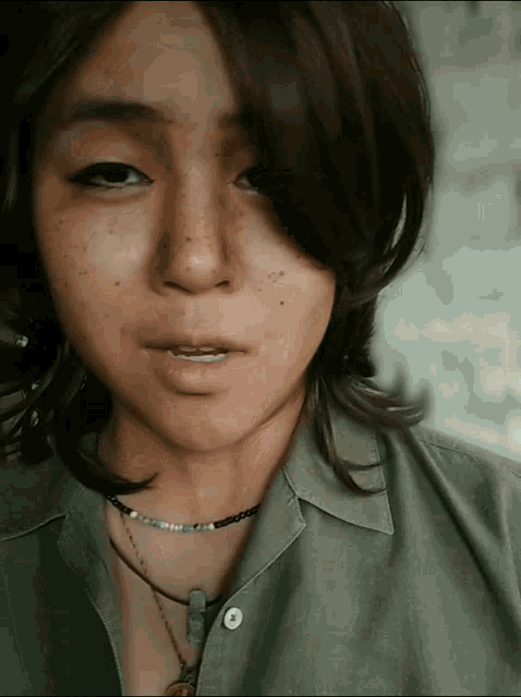 a close up of a woman 's face wearing a necklace and a green shirt