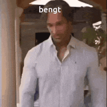 a man in a blue shirt is standing in a hallway with the word bengt written on the bottom of his shirt .