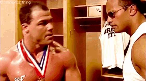 two men are standing next to each other in a locker room . one of the men has a medal around his neck .