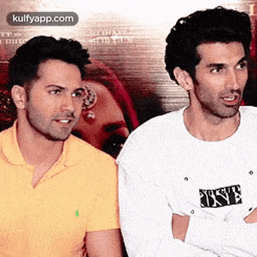 two men are standing next to each other with their arms crossed . one of the men is wearing a yellow shirt .