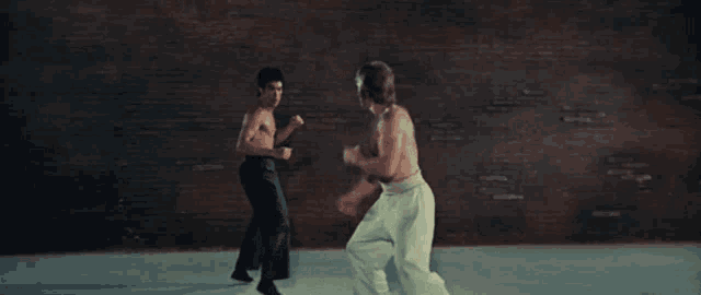 two men are fighting in a room with a brick wall in the background .