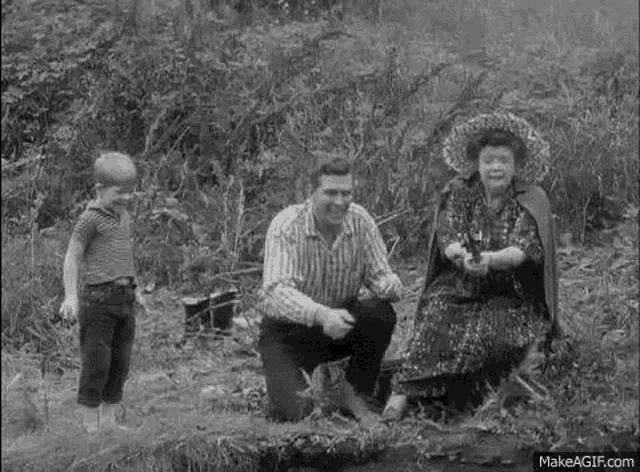 a black and white photo of a man kneeling down next to a woman and a boy .