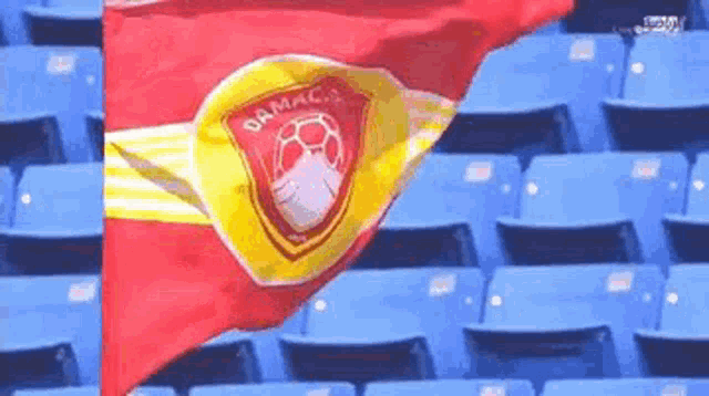 a red and yellow flag with the word damac on it is waving in a stadium