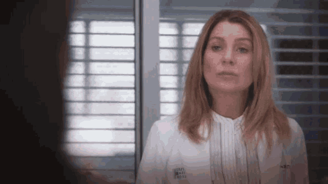 a woman in a lab coat is standing in front of a window in a hospital room .