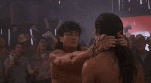 a man without a shirt is fighting another man in front of a crowd of people