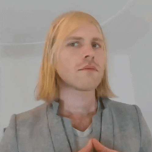 a man with long blonde hair is wearing a grey jacket and white shirt