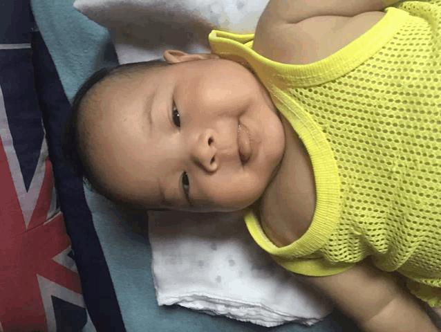 a baby in a yellow tank top is smiling on a bed