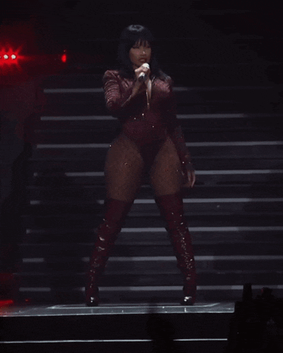 a woman in a red bodysuit and red boots is singing into a microphone on a stage