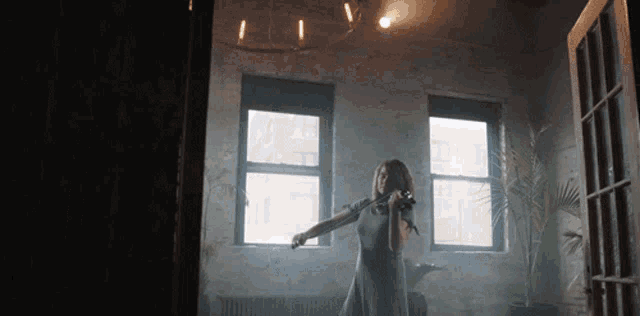a woman is playing a violin in a room with windows