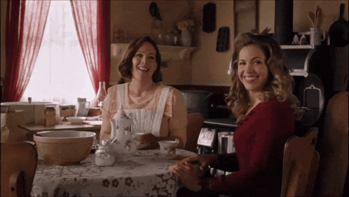 two women sit at a table with a bowl and a pitcher