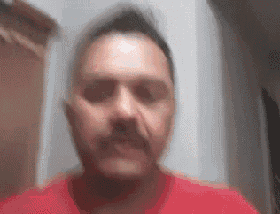 a man with a mustache is wearing a red shirt and making a funny face .