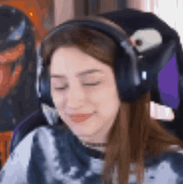 a woman wearing headphones and a tie dye shirt is sitting in a chair with her eyes closed .