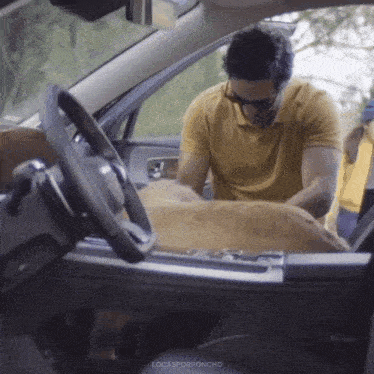 a man in a yellow shirt is sitting in a car with a dog in the back seat