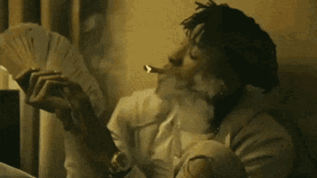 a man is smoking a cigarette while holding a fan of money in his hand .