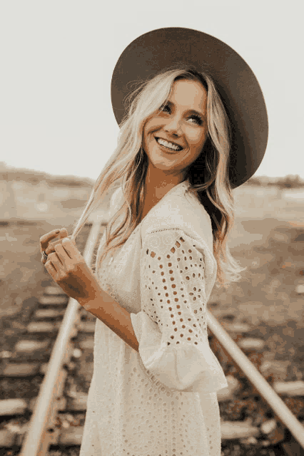 a woman wearing a hat and a white dress is smiling
