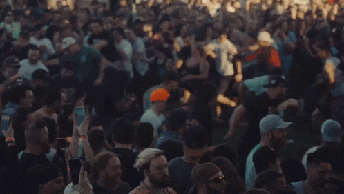 a crowd of people are dancing at a concert and taking pictures with their phones .