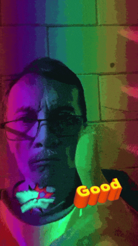 a man with glasses is surrounded by a rainbow of colors and the word good is on the bottom right