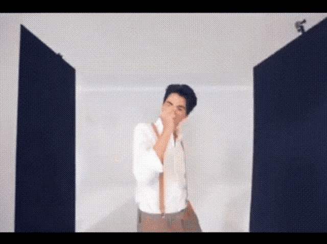 a man in a white shirt and suspenders is standing in front of a door covering his mouth .